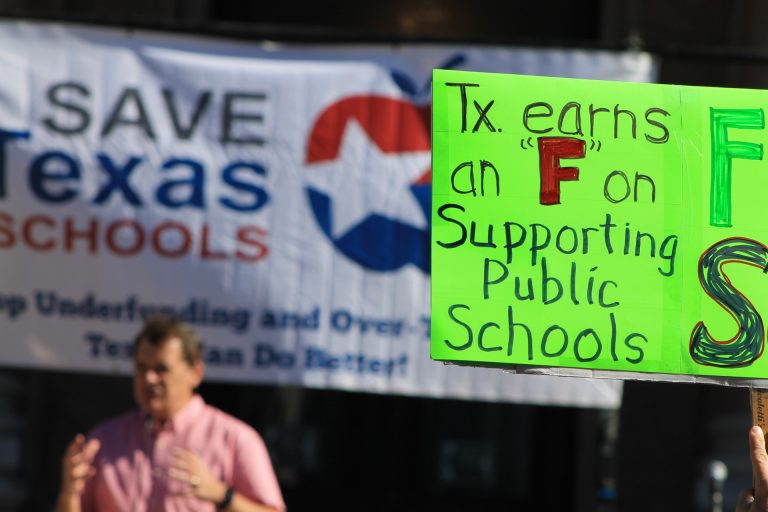 At the Save Texas Schools rally at the Texas Capitol on March 25, 2017,  a speaker calls on Lt. Gov. Dan Patrick to fix the Robin Hood system. One sign holder gives the legislature a grade for its efforts to support public schools. The issue is still relevant for the current legislative session. Photo by Kathryn Chilstrom.