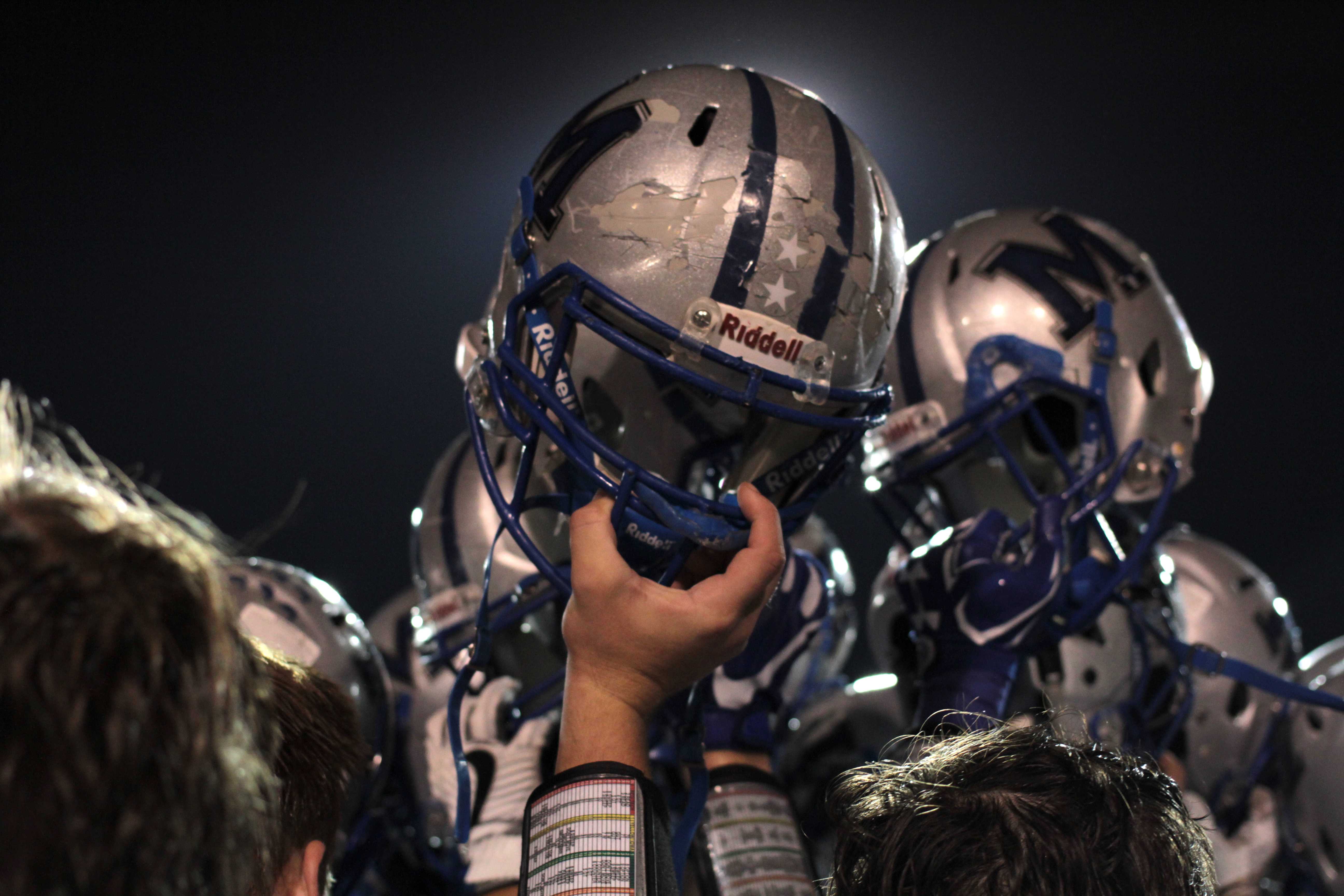 HARD HATS: In the final post-game huddle, players raise their battered helmets to the sky. Photo by Ian Clennan