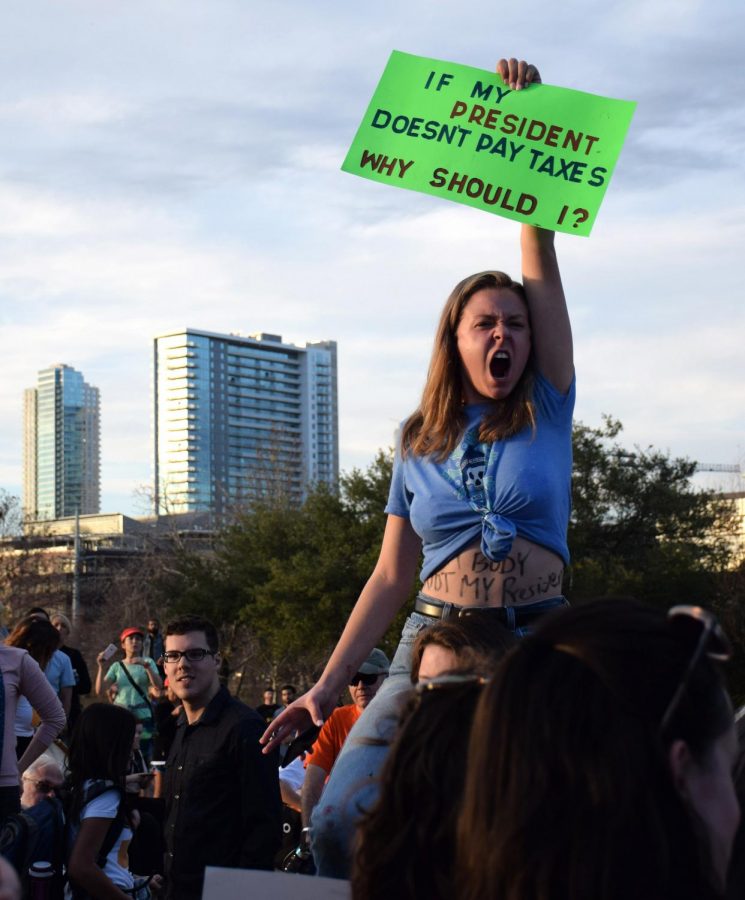TAXING HER PATIENCE: Senior Bella Cude brandishes a sign that criticizes President Trump’s refusal to release his tax returns while wearing another protest message—”My Body, Not My President”—across her stomach. As many as 200 McCallum students walked out of school on Inauguration Day at the start of fourth period to join the thousands of protestors who assembled at Auditorium Shores. “It was really liberating and empowering to see everyone rally over one cause,” Cude said.  Photo by Grace Brady.