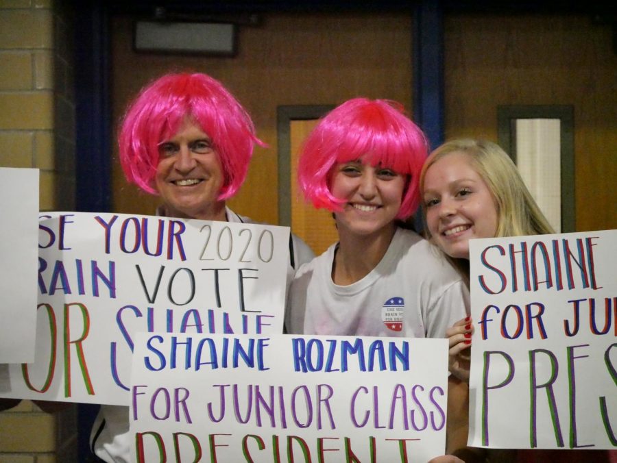 Shaine Rozman and her older sister, or perhaps it is actually principal Mike Garrison, don pink wigs for Pink Night and join senior Claire Caudill in advertising Rozmans candidacy for junior class president. Photo by Ale Luera.