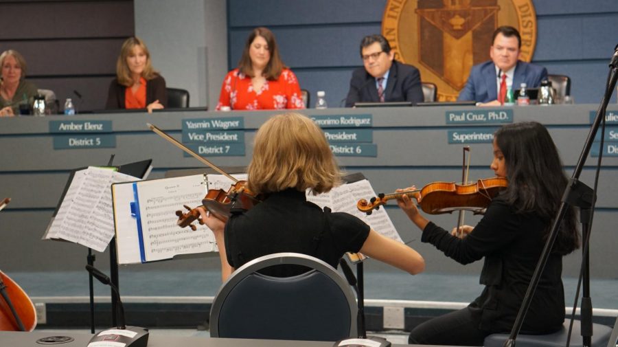 Lucy Harme (left) and Kavya Srinivasan (right) play their violins during their orchestra performance as the board watches and listens.