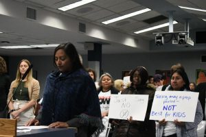 Those in protest of the potential budget for the 2019 school year hold signs during public comments directed at the school board trustees at a Nov. 26 meeting.