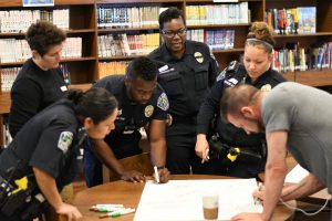 Austin Police Department officers work together to respond to a poster activity. The roundtable participants wrote down their perceptions of teenagers and police officers and then came together to discuss those perceptions. Photo by Bella Russo.