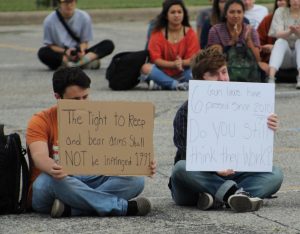 Defending the rights of gun owners at the McCallum walkout in support of stronger gun control legislation on April 20, 2018, three McCallum seniors (two of them pictured here) sit  silently counter-protesting at the rally in the parking lot. “I believe in the Second Amendment since it was instituted in the beginning of this country, one of them said. I obviously don’t believe in fully automatic weapons. They aren’t legal anyways. I’m pro-rifle, pro-gun and I’m pro Constitution.” One of the students asked to remain anonymous to protect future opportunities. Photo by Kien Johnson.