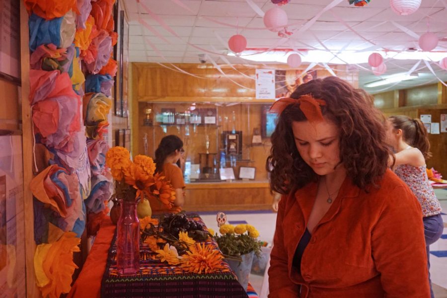 A WORLD OF COLOR: Sophomore Kiera Boehle focuses on the Day of the Dead altar that she was setting up as a part of Art Society volunteer work in the main hall on Thursday, Oct. 24. The altar displayed photographs, trinkets, flowers and other decorations honoring people that have died. “We made it all nice,” Boehle said. “That’s one of the reasons I like Art Society, it contributes to the art community and allows you to experience the world even when you’re in such a small space like a high school.” Photo by Lily Wilson.