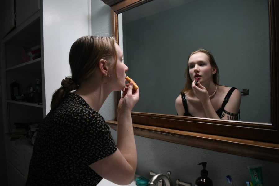 THROUGH THE LOOKING GLASS: Junior Ellen Fox looks upon on a Roaring 1920s reflection of herself in the mirror. The reflection flaunts the staples of  the time period: a flapper dress, a pearl necklace, and red lipstick. In the modern 2020’s version, she wears modern equivalents; a Madewell dress, hoops, a scrunchie and Chapstick. Original photos and digital illustration by Ellen Fox. 