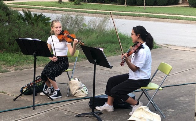 Lucy Hamre (left) and Ileana Nicholson (right) share a knowing look as they preform their violin arrangements for a socially-distanced audience. The profits from the performances went entirely to charities and organizations.  “It just felt really fitting that we do something that has monetary value to help organizations, Nicholson said. 