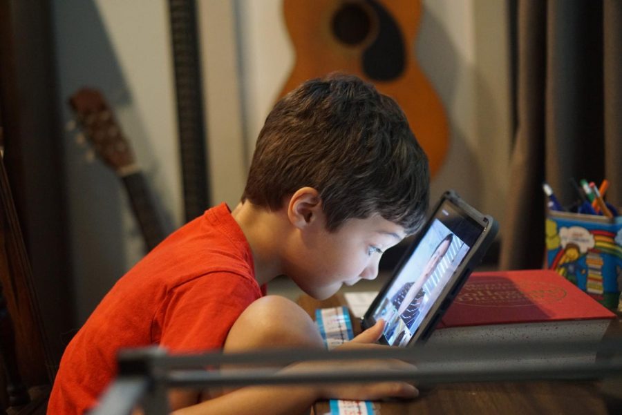 TAKING A CLOSER LOOK: Nate Baugh earnestly peers at his first-grade friends during a Zoom call regarding rhyming words and syllables. The way Nate sees it, school just isn’t the same without seeing his friends in real life.  “I wish my friends Griffyn and Caleb would zoom through the Zoom and out through my computer,” he said. “But I’m only left with this sausage!” Nate punctuated this sentence by holding up a piece of sausage from the kitchen and giggling so hard he nearly fell over. Photo by Madelynn Niles. 