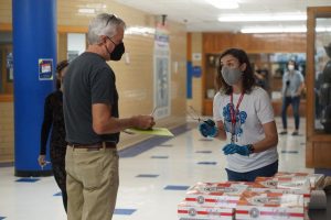 Wearing surgical gloves and using metal tongs, new facilities manager Camille Nix asks math teacher Scott Pass if he wants a glazed doughnut, a chocolate glazed doughnut or both. The sweet Friday treats came courtesy of the Mac administration.