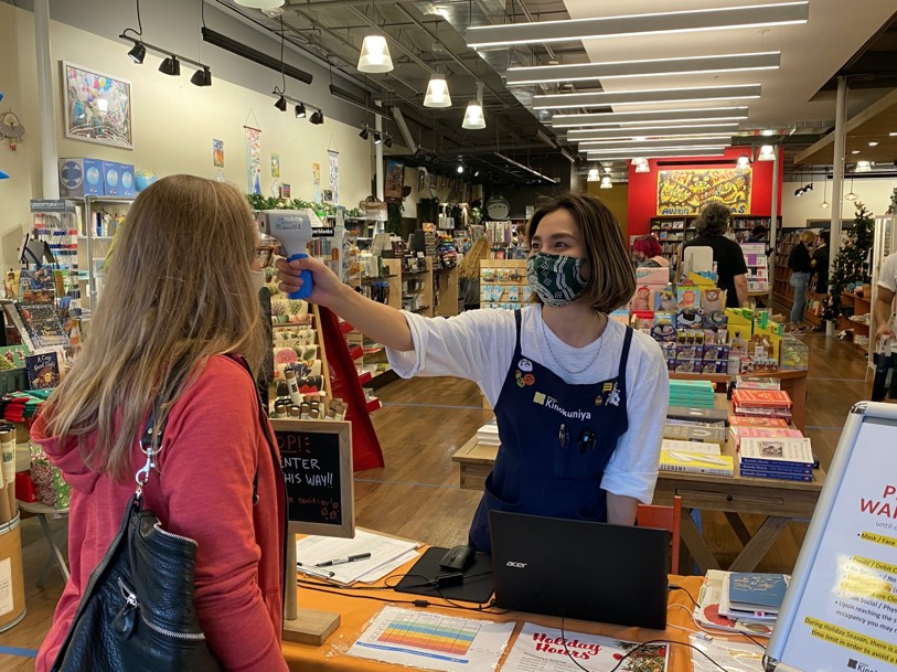 Shopping safely: Kinokuniya is a Japanese book and gift store that has been taking many COVID precautions these last few months, including a mandatory shopper temperature check at the entrance to ensure the safety of their customers. Pictured here, a Kinokuniya worker checks the temperature of customer Jenny, who said, “I feel safer knowing that the store is being so careful.” A sign at the door lists all of the store’s COVID precautions and rules, stating that “during holiday season, there is a 20-minute shopping time limit in order to avoid a long wait outside.”