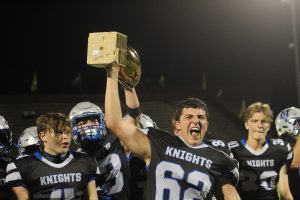 Senior center Braeden Price hoists the Taco Shack Trophy after the Knights 14-13 victory over the Trojans allowed the Knights to bring the cherished golden football to Sunshine Drive for the first time since 2018. 