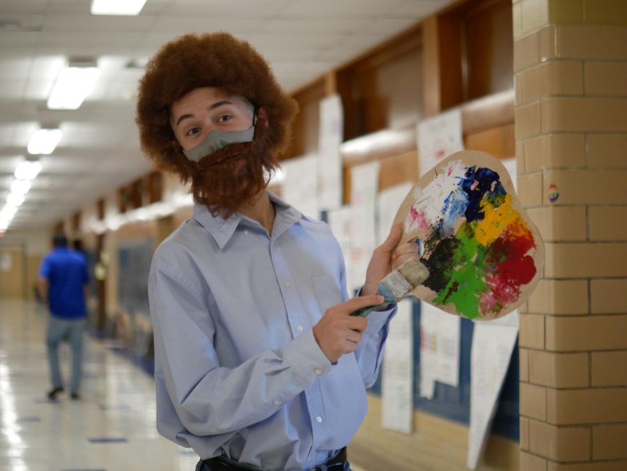 A BRUSH WITH GREATNESS: Inspired after seeing a Bob Ross costume on the HBO show Euphoria, senior Gage Sanchez decided to dress up as the iconic celebrity artist for several reasons: the costume was funny, festive, easy to take on and off and reflected his identity as an art kid who loves to paint. The costume may have been easy to wear, but it wasn’t easy to make. Sanchez already had the pants, the belt and the paintbrush, but he thrifted the oversized button-down shirt at Goodwill for $5 and bought the wig and beard from Party City. He then attached the beard to an elastic strap so he could remove it easily, and he cut the artists pallet from scrap wood with a jigsaw. It may seem like a lot of work, but Sanchez says that’s what it takes to get into the spirit of the holiday. “Buying a costume is so much more expensive, plus they all look sort of cheap, so I definitely love to resort to a homemade costume, plus making a costume at home using things from thrift stores or crafts can be really easy. ... It’s all part of the game in my opinion.” Coming to school as Ross was a far departure from the Voo-Doo Doll costume for which he won Scariest Costume in the art society’s 2020 virtual costume contest. The Ross costume it turns out was just Sanchez’s costume for school. He made his “real deal” costume, Tate from American Horror Story, to wear to a party. It took him six hours.