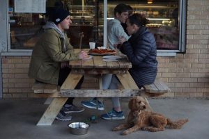 ANONYMOUS PIZZA ENJOYERS: Two unidentified diners and their dog, Waffles, sit at a picnic table in front of Little Deli, a pizza restaurant in the heart of Crestview. Little Deli, originally a sandwich shop, added a pizza kitchen to the business in 2009 and has been attracting huge numbers of customers for years. “It’s a great gathering spot for the community,” one of the diners said. Photo by Camilla Vandegrift.