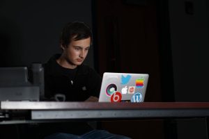 Senior Holden Satterwhite, CEO of Redfruit Media, works on his computer adorned with his collection of stickers–including his own Applelosophy logo. 