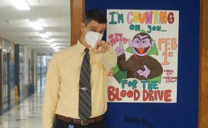 COUNTING ON YOU: 
Posing next to a poster advertising the blood drive made by senior and PAL Marina Garfield, the Count, also known as statistics teacher Richard Cowles, was Bram Stoked for this year’s blood drive on Feb. 1.  The Count has been lurking the hallways of McCallum for at least nine years, but his origins date back to Cowles’ college days.
Being a math teacher, of course, I’ve always liked Count Von Count,” he said, “but my college job was cooking at Chili’s, and I would have to call down to the grill and say I need one grilled chicken! Ha, ha, ha! It became a habit, and since vampires and blood go together, I kept it up and people seem to like it here.” (Editor’s note: previous quote must be read in Transylvanian accent.)