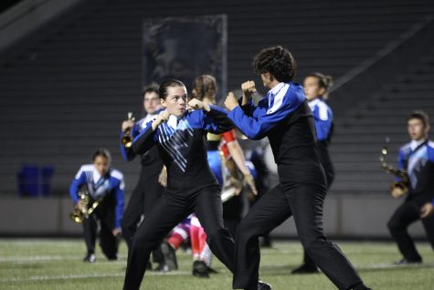 ROLL WITH THE PUNCHES: Seniors Mira Wagner and Tyler Mankinen duke it out during the first moments of the final round at the Cap City Marching Competition. The 2022 marching show “Seeing Stars” gets its name from its boxing theme, and according to Wagner, who represents the woodwinds section, the early fight scene “definitely sets the tone.”

“Right off the bat you see two people fighting so you know that this show is full of energy,” Wagner said.”  “Even throughout the show the woodwinds and brass are ‘competing’ against each other which goes with the boxing theme.”

Mankinen, who represents the brass section, believes the fight scene is a crucial element in the marching show. 

“[The fight scene] usually gets the crowd pumped up and draws the attention of the audience into the show,” Mankinen said. “The show is super unique and seeing the crowd react to an unconventional element of a marching show is really exciting.” 

Caption and photo by Morgan Eye.