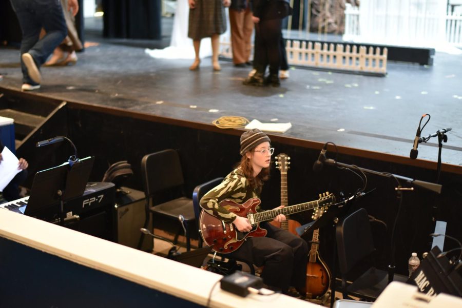 RENAISSANCE WOMAN: Junior Meredith Grotevant warms up before a dress rehearsal run of Pippin. Throughout the show, Grotevant plays five different instruments, including acoustic guitar, electric guitar, banjo, mandolin and ukelele for the pit orchestra. “

When I agreed to play in the pit, I thought I was just playing guitar,” Grotevant said. Then the next day I was in jazz band and Ms. Nelson came up to me and she said ‘So the thing is, there are five different instruments on the book.’ She started listing them and I realized that I had at least a little bit of experience playing all of them. It was a little bit scary at first because guitar is my main instrument and I’m not professional with the other ones, but I had them all at home and I was more than willing to learn.”

Last year, Grotevant had intended to be in the pit orchestra for the spring musical Joseph and the Amazing Technicolor Dreamcoat, but the production decided against having a live orchestra due to COVID safety concerns. This year, Grotevant made sure to be involved.

“Last year I learned half the music over the winter break and then when we got back, they said therell be no pit due to COVID,” Grotevant said.  “So that was a little bit of a bummer, but I was really excited for whatever the spring musical was going to end up being this year. I really wanted to see what being in the pit would be like. I like to try new things and expand my musical abilities and I thought that this would be a really good opportunity to be in like high-quality production with MacTheatre around a bunch of other great musicians doing something fun.”

Reporting by Alice Scott. Photo by Noah Braun. 