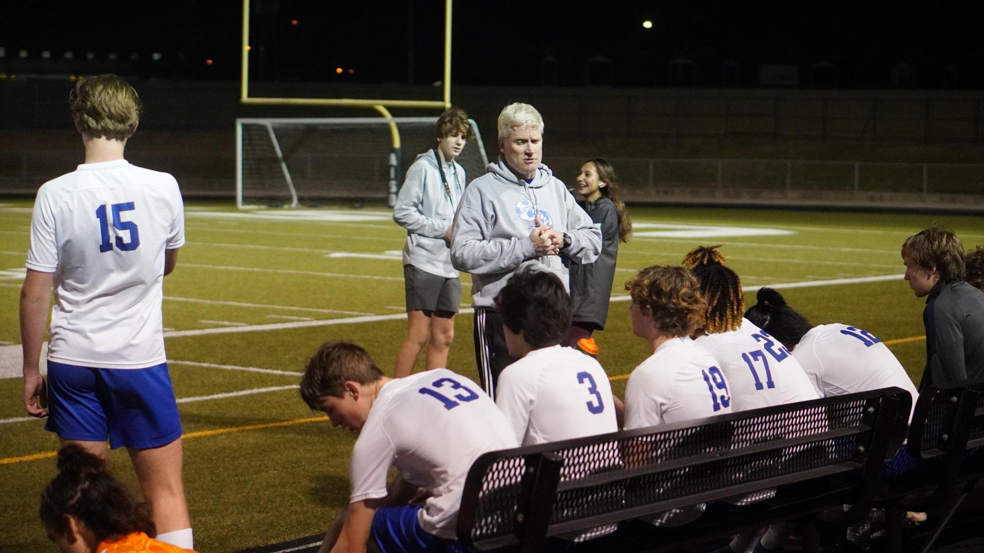 Coach Nick Martin speaks to the varsity soccer team during half time.