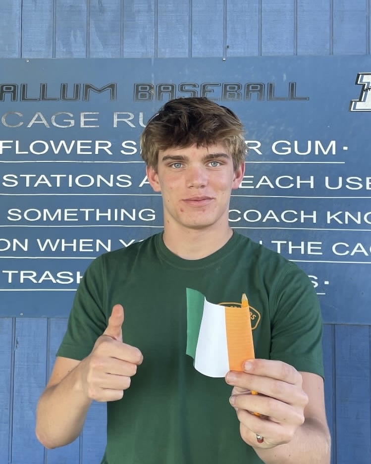 Senior Gabe Scheibal holds up an Irish flag in front of the McCallum Baseball sign., representing the Irish college Scheibel has accepted admission to in the fall, Trinity College Dublin. 