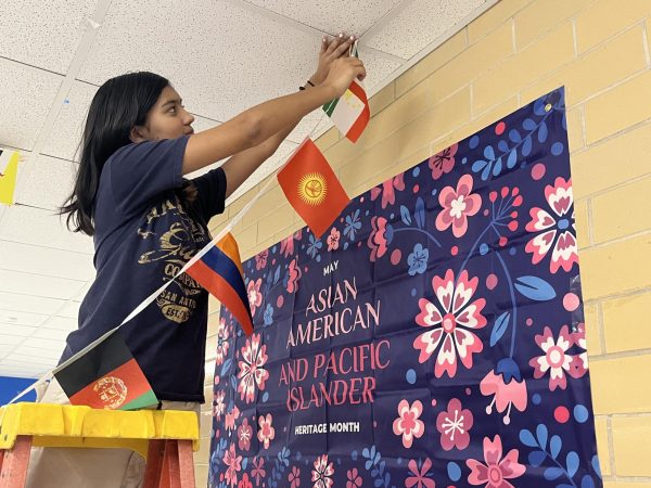 Freshman Tegan Hahn installs flags above the main hallway as part of the Students of Color Alliance's efforts to observe Asian-American and Pacific Islander Heritage Month. Hahn shared that it's been a big adjustment coming to Mac, which has relatively few Asian-American students compared to her middle school, Canyon Vista Middle School in north Austin, where Asian-American students are the largest group in the student body at roughly 40 percent of the student population. 