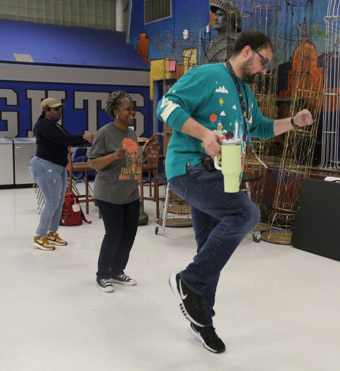 Even with a water bottle in his right hand, a walkie-talkie clipped to his belt, a lanyard around his neck and a winter holiday Disney sweater on, Fine Arts director Dr. Samuel Parrott is still able to bust a respectable move as SCORES teacher Helaine Brockington and Fine Arts Academy assistant Tonya Moore line dance alongside him.