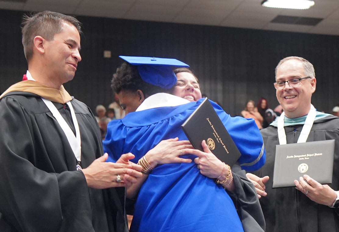 College and career counselor Camille Nix takes advantage of her preferential seating at graduation, moving between superintendent Matias Segura and principal Andy Baxa so she can greet senior Terron Hall as he receives his diploma at the McCallum commencement ceremony at the Burger Activity Center on May 30. Nix said that Hall came to Room 130 every morning to deliver a similar hug and morning greeting to Nix. He is the most kind kid in the world, Nix told the Shield. He is pure joy.