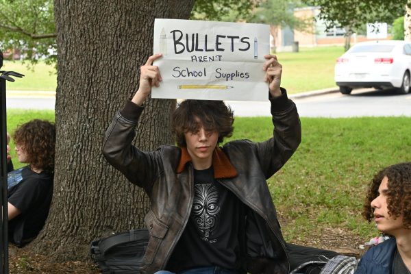 TAKING ACTION: The photo above was from the 2023 statewide gun control walkout. Now alumni, Zephan Mayeda leans against a tree during the walkout holding a sign reading “Bullets aren’t school supplies.” He participated in the walkout to protest against the lack of gun protection in the U.S. and to draw attention to the statewide protest. 

“Children are dying due to government’s apathy and corporate lobbying against any action of any kind,” Mayeda said. 

Mayeda was disappointed in the lack of organization that came with the protest but still participated. 

“Better something than nothing,” he said. 

Mayeda offered what he would love to see at the walkout.  

“I would have loved to see marching, chants, speeches, lists of phone numbers to call senators, names pictures and birthdays of the victims, flyers promoting the protest days weeks or months even in advance, mass absences, an actual walkout for those who can’t not go to school that isn’t just 20 minutes of sitting,” Mayeda said.

Although he was underwhelmed, Mayeda appreciated the symbolism. 

“I think it held some importance in regards to symbolic gestures,” Mayeda said. 
Reporting by Kate Boyle.