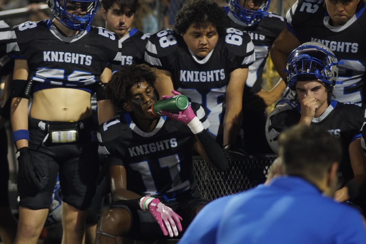 Senior wide receiver CJ Forbes hydrates while his coach addresses the team during a break in the varsity football team's game against Elgin on Friday, Sept 20.