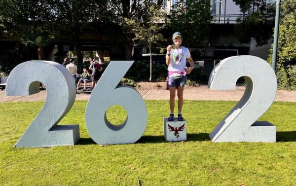 Lynn Bucknall holds her medal, standing on 26.2 sculpture after finishing the Portland Marathon 