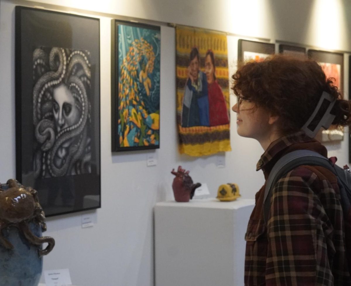 WISHFUL WINDOW SHOPPING: Senior Mia Plemons observes the displays in the MAC during the 5x7 gallery night. Although not a member herself, Plemons feels a connection to the program through her friends and peers. “I have a lot of friends in art,” Plemons said. “And I’ve seen a lot of their work and it’s all really nice and beautiful, and I really enjoy seeing some of the nice pieces people have made.” Plemons didn’t manage to secure a piece of her own, but left impressed by all the ones she saw. “I didn’t [have a favorite], every piece of art I saw was just absolutely breathtaking,” Plemons said. “I think they should definitely do more things like this in the future. I think it’s definitely great for people in the art program to get their art out there and getting experience with making things that people buy.” Caption by Noah Braun. Photo by Lilah Lavigne.