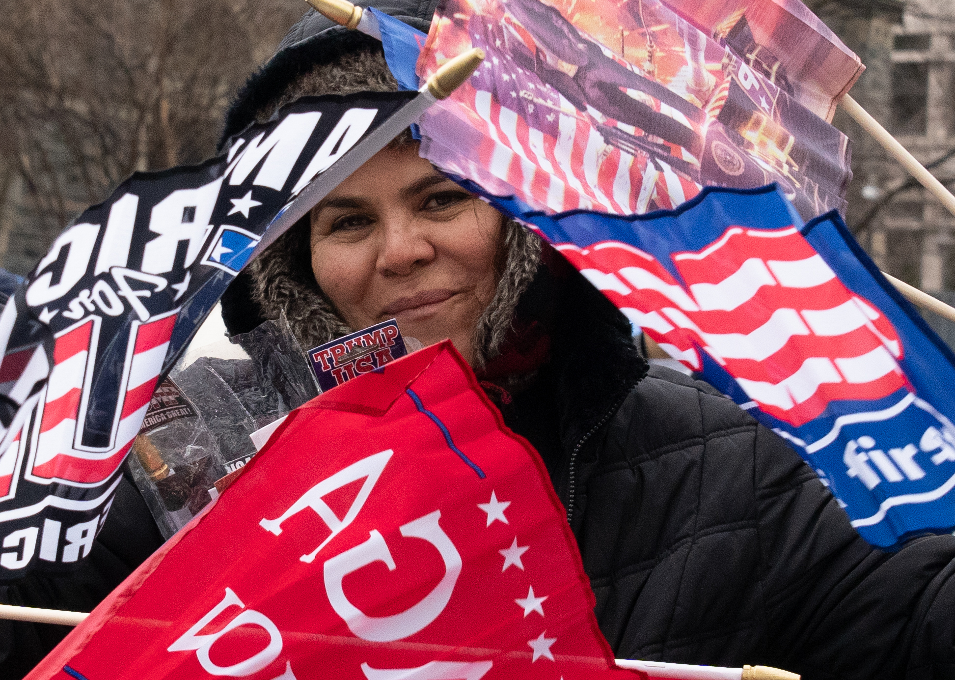 Outside the Trump inauguration rally at the Capitol One Arena, a fan celebrates with flags surrounding her, the day before the Inauguration. This photo was taken three hours before the rally actually began, so this person had already been waiting a long time, much of it in the rain. Photo accessed on the Flickr account of Victoria Pickering. Reposted here under a creative commons license.