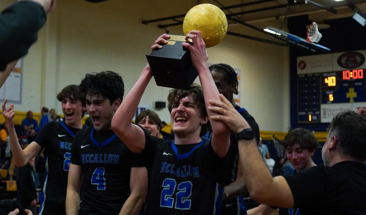 Senior George McCoy celebrates after scoring his 1,000th career point on Jan. 24 at Anderson. The varsity boys basketball team completed a season sweep with a 60-40 victory against the Trojans that also allowed them to keep the Taco Shack Shields Collide trophy that they have brought home all three times the new rivalry trophy has been at stake. About four and a half minutes into the third quarter, McCoy was just one point away from 1,000. After an Anderson 3-pointer that cut McCallum's lead to six, senior Tommy Ammerman took back possession of the ball and passed to McCoy. McCoy then dribbled the ball downcourt, avoiding two Anderson defenders before pausing to take a 2-point shot from the paint. As the ball floated through the air towards the basket, the gym was nearly silent for a moment. When the ball swished through the hoop, however, the Anderson gym returned to its typical noise level as McCallum students, parents, coaches and basketball players erupted in celebration. Caption and photo by Julia Copas. 