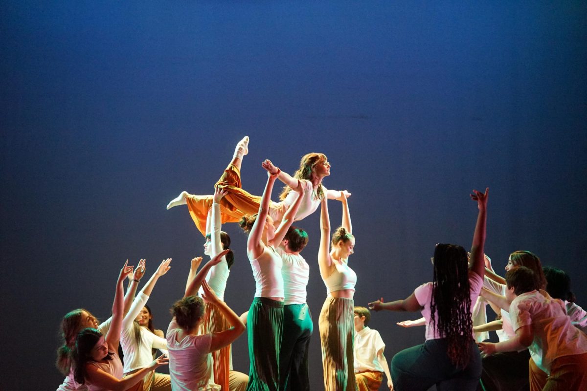 A SEASON OF DANCE: Freshman Dance I student Alina Curtin (bottom left) reaches her arms up toward freshman Susan Welsh as her fellow dancers lift Welsh into the air in “As Seasons Change”, a contemporary piece choreographed by Curtin. 

Although Curtin wasn’t physically involved in the lift, she had an important role in communicating the dance’s symbolism. 

“I am reaching my arms up to Susan,” Curtin said. “It is supposed to represent letting go of the past and how hard that can sometimes be.”

While Curtin enjoyed the lift, her favorite section of the dance was towards the end, where she performed two pique turns and a head roll for four counts. 

“It felt very freeing and was a moment for the dancers to breathe and focus more on performance rather than stress about technique,” Curtin said.

Curtin said she was grateful for the creative freedom to choreograph the pique turn series and other sections within the dance.

“Getting to create a dance is a rare opportunity, especially for beginning dancers,” Curtin said. The fact that our teacher trusted me with that meant a lot. It made this dance feel like my baby–my special thing that I got to share with both friends and the audience.”

Curtin said it was also cool to see how her fellow Dance I student’s sections of the dance came together with hers to create the final piece. 

“Getting to explore my own dance skills and see how the styles of all the different creators was really fun,” Curtin said. “Each of our sections had very different vibes yet somehow came together. I was amazed about how that could happen.”

Aside from the piece itself, Curtin said she is grateful for the dance community at McCallum because of how supportive and welcoming they have been.

“Everyone is cheering and people watch from the wings waiting to give you a good job hug right when you walk off,” Curtin said. “People may think dance is scary and everyone is mean but at McCallum that could not be further from the truth.”

Caption by Elizabeth Nation. Photo by Sophia Manos.