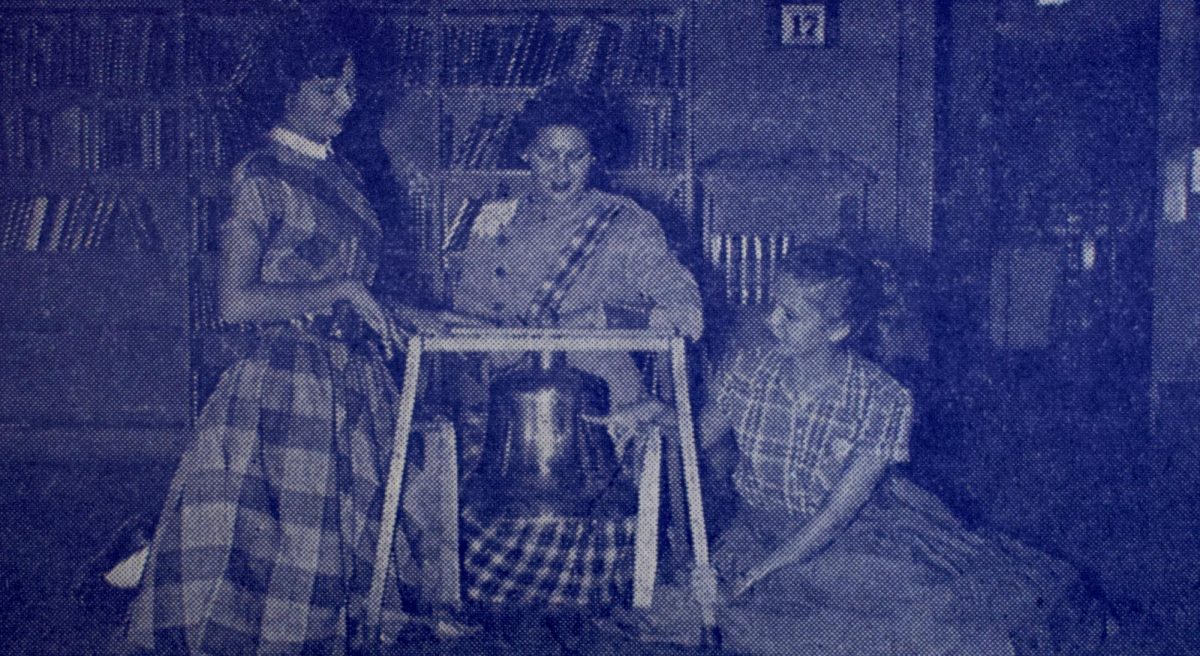 Laneta Stefka (Knight Editor), Ann Kinch (Blue Brigade President), and Jo Eickmann (Shield Editor) admire the Victory Bell in its habitat of last year, the Travis High library. Eickamann is pointing out a previous McCallum victory which the Knights hope to duplicate in tonights McCallum-Travis game. Caption and photo by 1957 Shield staff. 
