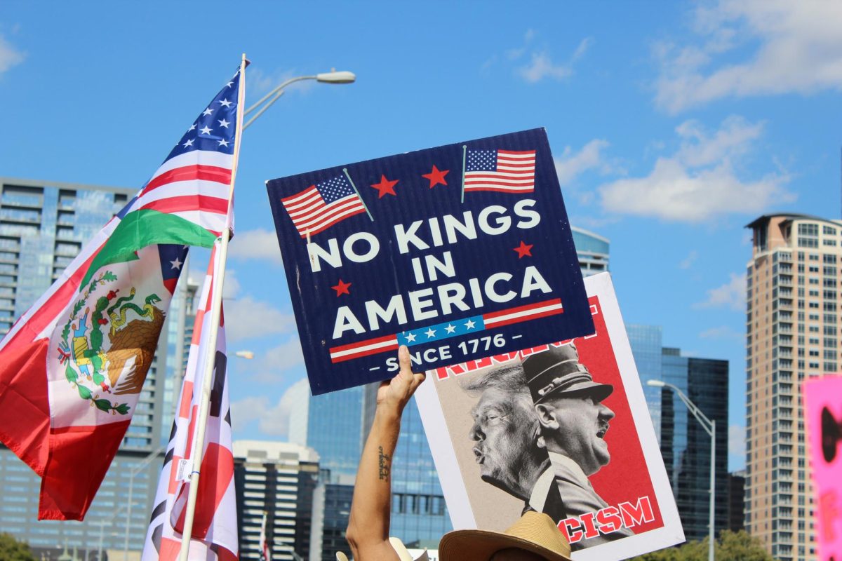 A protester holds a No Kings sign up as Mexican and American flags share the Austin skyline.
