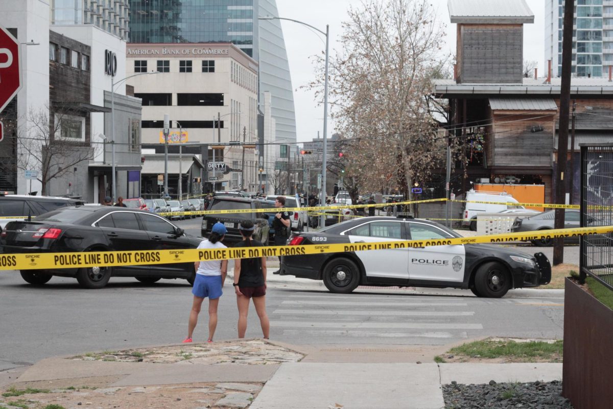 Onlookers watch police investigation of the shooting scene on West Sixth St.